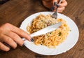 Woman hand holding fork and knife with spaghetti bolognese in white plate on wooden table. Royalty Free Stock Photo