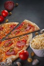 Italian homamade pizza with one piece and ingredients. Italian pizza on a dark gray black background