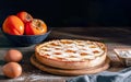 Italian homemade persimmon tart or crostata with ingredients on the wooden table, chiaroscuro