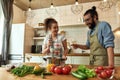 Italian man, chef cook holding a glass of wine while woman using hand blender. Cheerful couple preparing a meal together Royalty Free Stock Photo