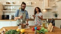 Italian man, chef cook using hand blender, preparing a meal while his girlfriend, young woman in apron pouring two Royalty Free Stock Photo