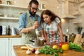 Italian man, chef cook using hand blender while preparing a meal. Young woman, girlfriend in apron looking at the Royalty Free Stock Photo