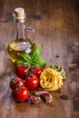 Italian and Mediterranean food ingredients on wooden background.Cherry tomatoes pasta, basil leaves and carafe with olive oil. Royalty Free Stock Photo