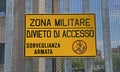 Italian military area with yellow sign: `Military zone, no entry, armed surveillance`.
