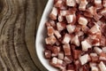Italian pancetta, bacon cubes, diced ham, cutted pork in square white plate on wooden textured surface