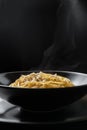 Italian pasta in a black plate. Hot pasta comes steaming from the cooked dish. Cacio e Pepe - Italian Pasta