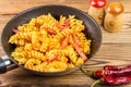 Italian pasta fusilli with tomato sauce and sausage in pan, red pepper on wooden table, space for text Royalty Free Stock Photo