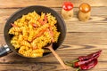 Italian pasta fusilli with tomato sauce and sausage in pan, wooden spoon, red pepper on table, top view, space for text Royalty Free Stock Photo