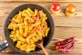 Italian pasta fusilli with tomato sauce and sausage in pan, wooden spoon, red pepper on table, top view, space for text Royalty Free Stock Photo