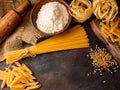 Italian pasta, spaghetti, fettuccine, penne, rolling pin, flour on a textured background. Top view