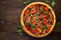 Italian pizza with ham, tomatoes, olives, cheese and scattered arugula on rustic wooden background. Royalty Free Stock Photo