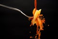 A drizzle of tomato sauce falls on a fork with the pasta creating many splashes on a black background