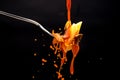 A drizzle of tomato sauce falls on a fork with the pasta creating many splashes on a black background