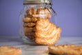 Italian puff pastry fan wavers cookies biscuits with preserving glass jar on marble table and lilac background Royalty Free Stock Photo