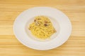 Italian recipe of spaghetti carbonara with guanciale on white plate and light wooden table