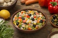 Italian rice salad with tuna in a brown ceramic salad bowl on a rustic wooden table with ingredients.