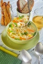 Italian soup with spaghetti, carrots, lemon, parsley and pieces of chicken in a green plate, on a table with napkins, spoons of Royalty Free Stock Photo