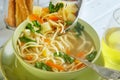 Italian soup with spaghetti, carrots, lemon, parsley and pieces of chicken in a green plate, on a table with napkins, spoons of Royalty Free Stock Photo