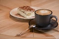 Italian stylish dessert, a piece of Tiramisu cake on a white plate and a cup of black coffee in a black cup on a table Royalty Free Stock Photo