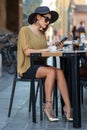 Elegant Italian woman with hat and glasses writes a message with her smartphone