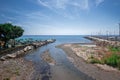 View of a Mediterranean landscape where a wide river flows into the sea, green trees on either side, a terrace on the beach.