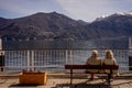 Italy, Menaggio, Lake Como, a group of people sitting on a bench in front of a mountain
