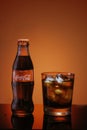 Italy, Milan - 15 November 2019: Classic bottle Of Coca-Cola and glass of fresh Coca Cola with ice cubes on red background