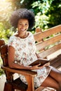 Its hard not to be happy when youre reading. Portrait of a young woman reading a book on a bench outdoors. Royalty Free Stock Photo