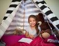 Its her own little reading nook. Portrait of a little girl reading a book with her teddybear in a tent at home.