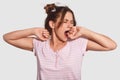 Its high time to go in bed! Sleepy young woman yawns, has tired expression, wants to sleep, dressed in nightclothes, isolated over Royalty Free Stock Photo