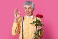 Its perfect. Photo of attractive mature man with grey hair, wears elegant yellow shirt, bowtie and suspenders, holds bouquet of