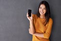 Its small but very smart. An attractive young woman holding up a mobile phone while standing against a gray wall. Royalty Free Stock Photo