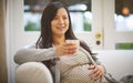 Its strictly decaf for a while. an attractive young pregnant woman drinking an iced coffee while relaxing on the sofa at