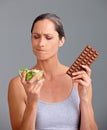 Its a really tough decision...Studio shot of an attractive mature woman deciding between a salad and chocolate.