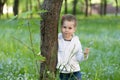 Ittle girl with a bunch of forget-me-nots in her hand peeking from behind a tree