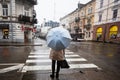 Ivano-Frankivsk, Ukraine - March, 2023: Back of woman with umbrella stand near pedestrian croos in rain street