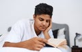 Ive been reading a lot lately. a young man reading a book while lying on his bed. Royalty Free Stock Photo