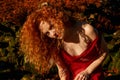 Ivory Flame. Woman with red hair posing against old bracken with wild curly hair across her face in a red dress