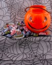 Creepy Pumpkin head collecting bucket with pile of Halloween sweets on a spider web background