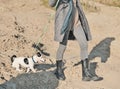 jack russell terrier dog on a leash walking with woman, crop view. woman wearing autumn outfit walking along sandy beach