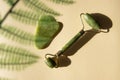 Jade Gua sha scraper and facial massager on beige background.