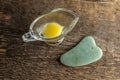 Jade scraper for gua cha and ghee in a glass cup on a background of wood