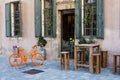 Orange bike, wooden table with stools, old building facade