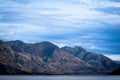 Jagged form of Remarkables Mountain Range across Lake Wakatipu without snow and shadows and light through overcast sky Royalty Free Stock Photo