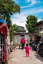 jakarta people and kids walking across the alley on a sunny day with blue sky and tree