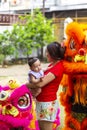 Jambi, Indonesia - January 28, 2017: Happy Asian mother holding baby posing next to lion dance performers doing acrobatics