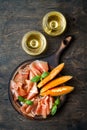 Jamon serrano or prosciutto with melon and wine in glasses over rustic wooden background. Italian or spanish antipasti