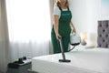 Janitor cleaning mattress with professional equipment in bedroom