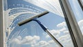 Window cleaning janitor using squeegee, wiping glass against bright blue sky with soft clouds overhead Royalty Free Stock Photo