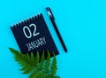 January 2th. Day 2 of month, Calendar date. Black notepad sheet, pen, fern twig, on a blue background